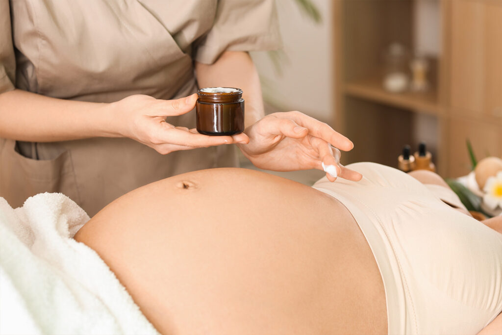 Therapeutin trägt pflegende Creme auf den Bauch einer schwangeren Frau auf